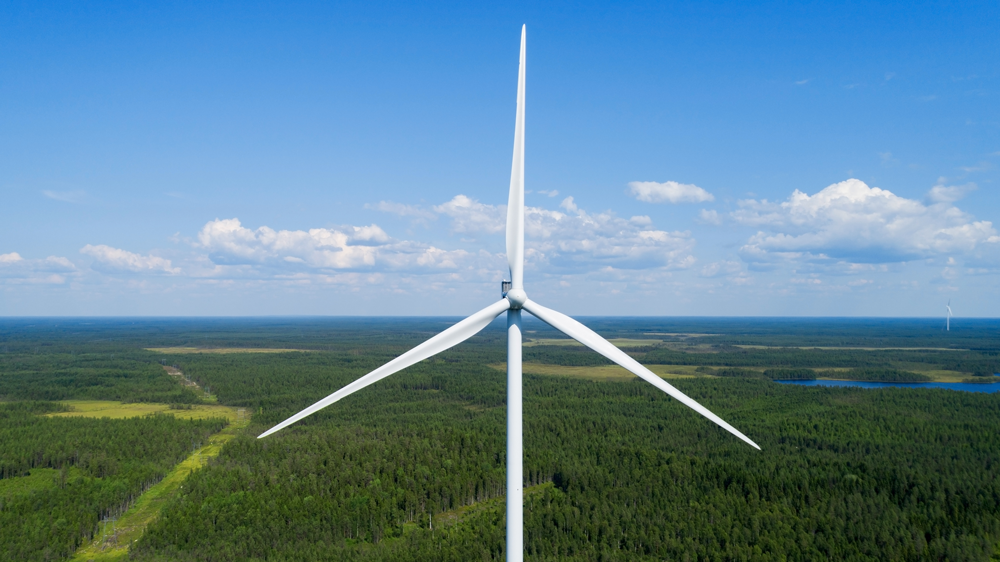 Wind turbine against a background of green forest and blue sky with clouds Wind turbine against a background of green forest and blue sky with clouds